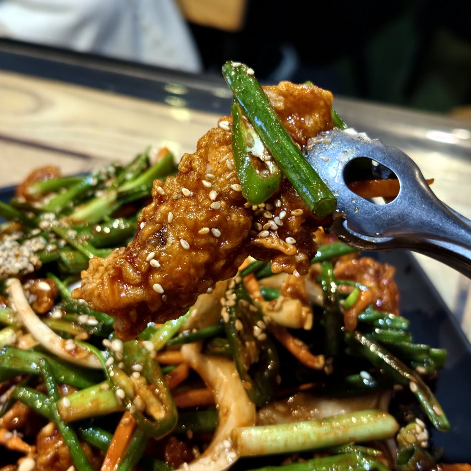 使用桌邊隨附的小鐵夾夾起軟嫩多汁的招牌青蔥蔬菜全雞肉塊,鮮味與肉汁滿溢