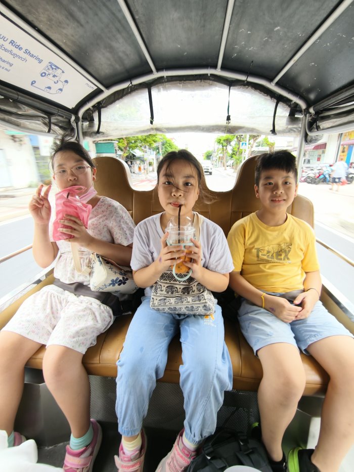 三位小朋友坐在MuvMi後座繫上安全帶喝泰奶，座位寬敞舒適