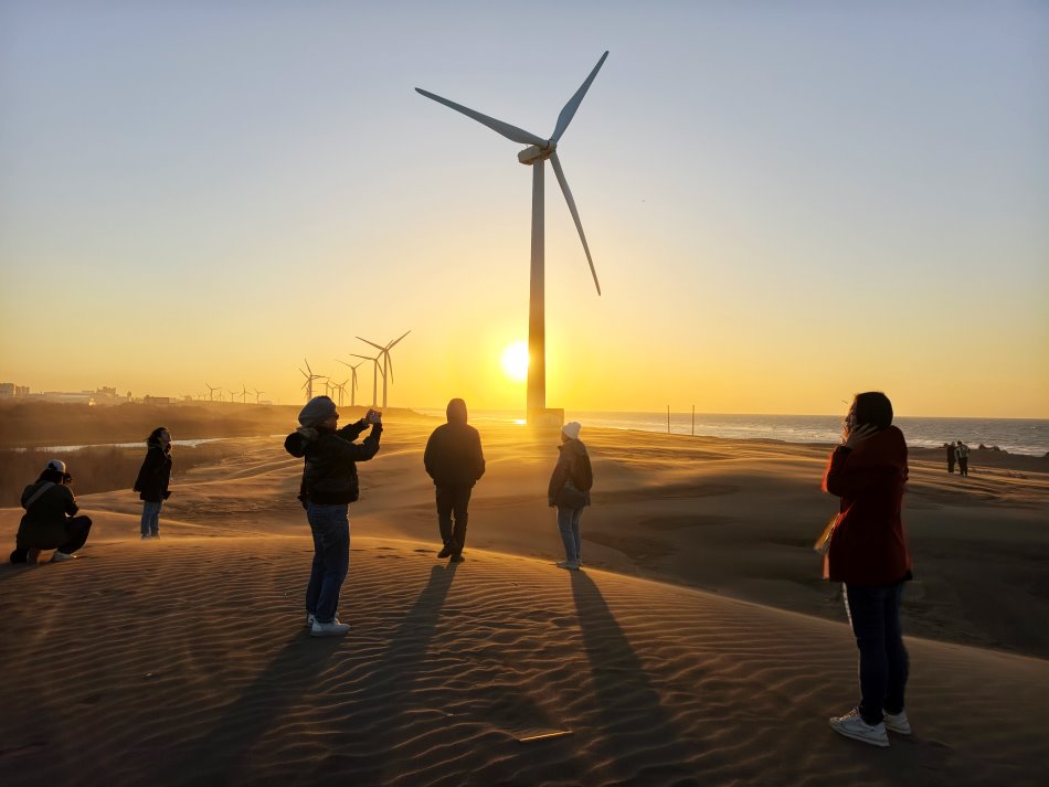 全副武裝防風帽口罩眼鏡的遊客在草漯沙丘夕陽前開心合影
