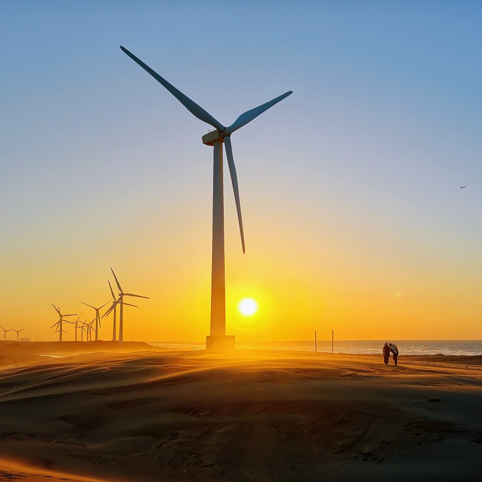 直幅構圖下的草漯沙丘高聳風力發電機與夕陽餘暉