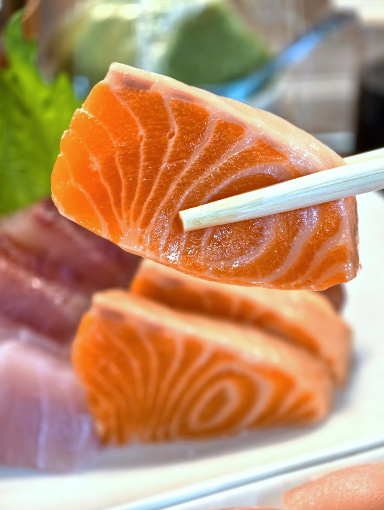 筷子夾起厚實鮭魚生魚片貝殼狀油花細緻